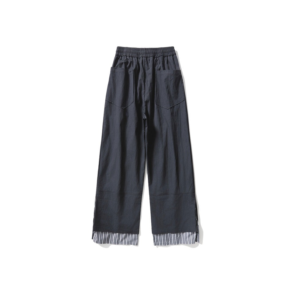 Back view of charcoal wide-leg trousers with an elastic waist, two patch pockets, and striped fabric at the cuffs.