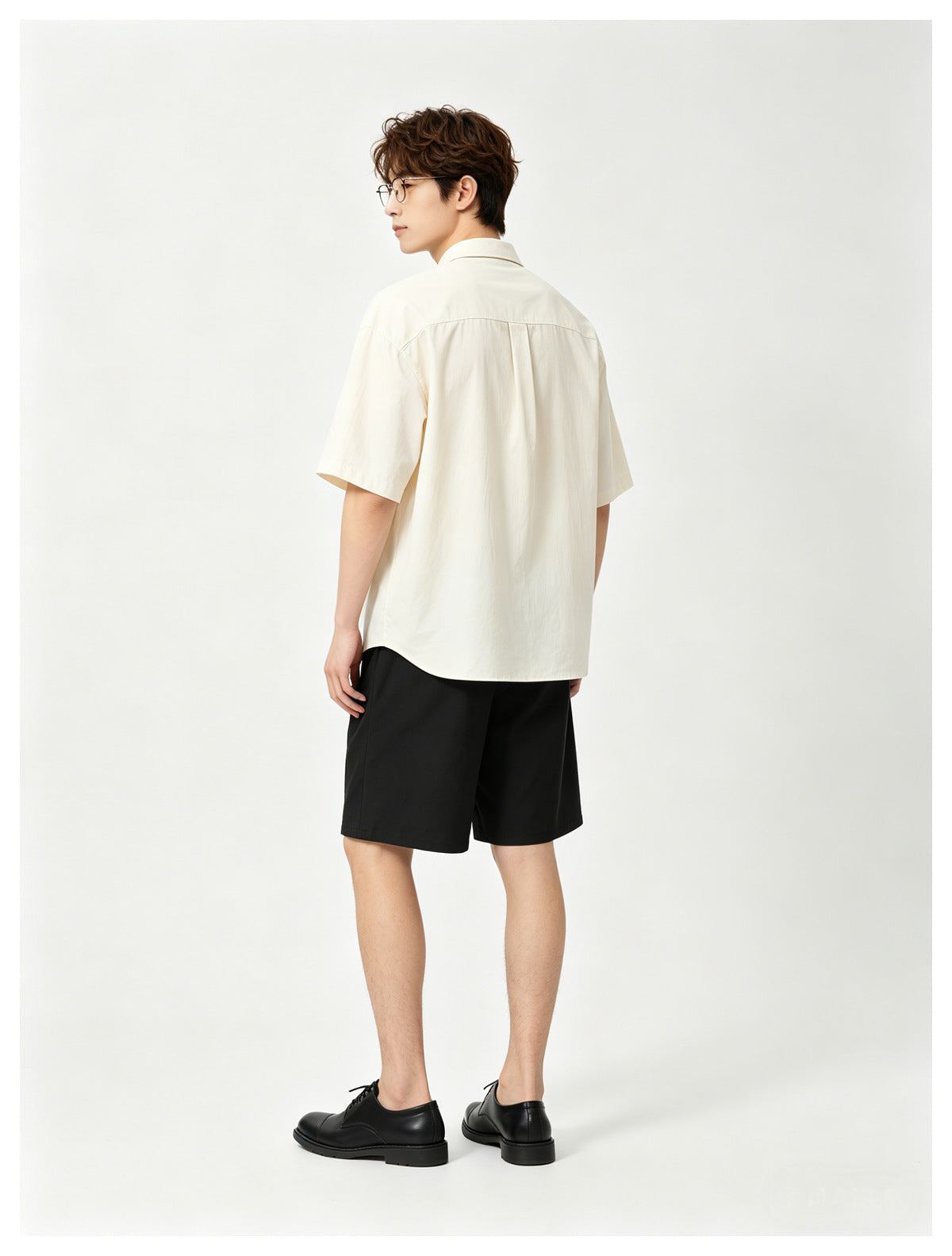 Rear view of a model wearing a cream short-sleeve shirt and black shorts.