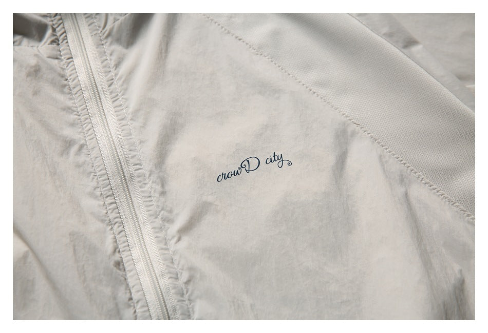 Close-up of the light beige jacket's zipper, textured panel, and small cursive chest logo.