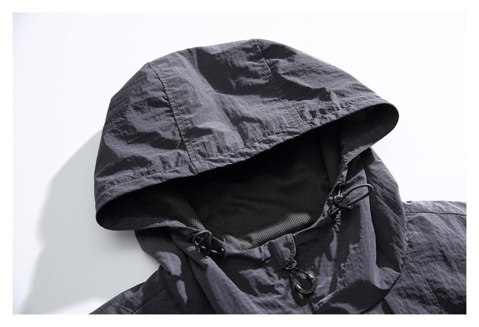 Close-up of a charcoal hooded jacket showing the mesh-lined hood, drawcord toggles, and zipper pull.