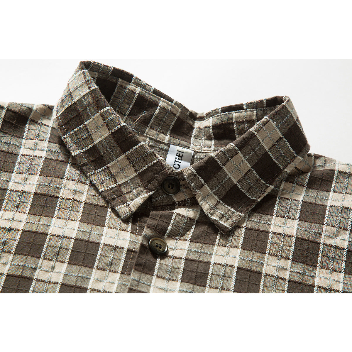 Close-up of a brown, beige and gray plaid shirt collar with dark buttons and a partially visible neck label.