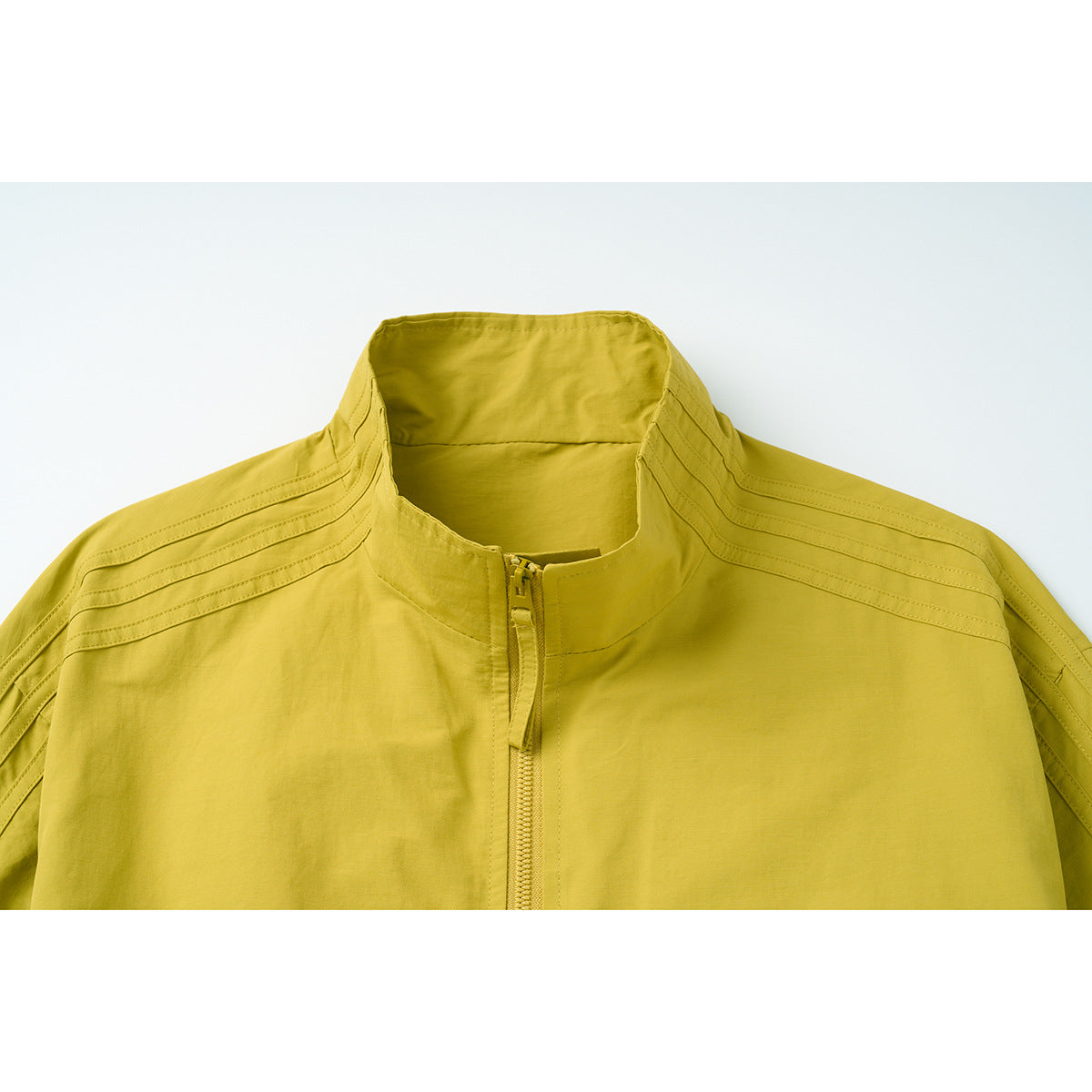 Close-up of a mustard yellow jacket with a stand collar, center zipper, and stitched shoulder panels.