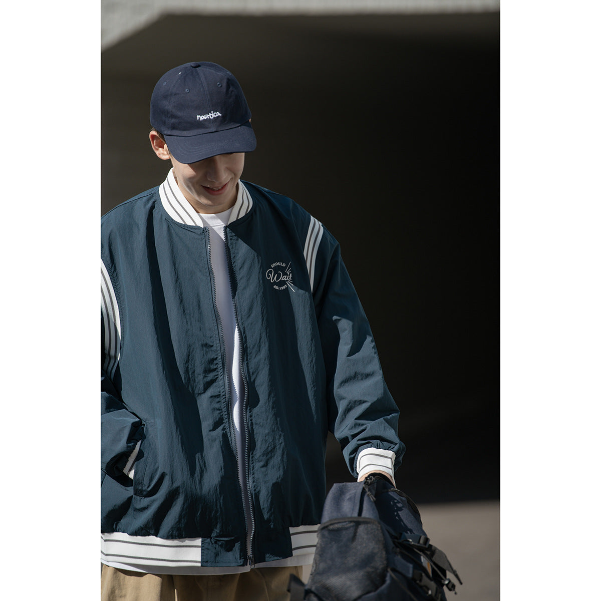 Close front view of a model wearing a dark navy zip jacket with white striped trim and a chest graphic.