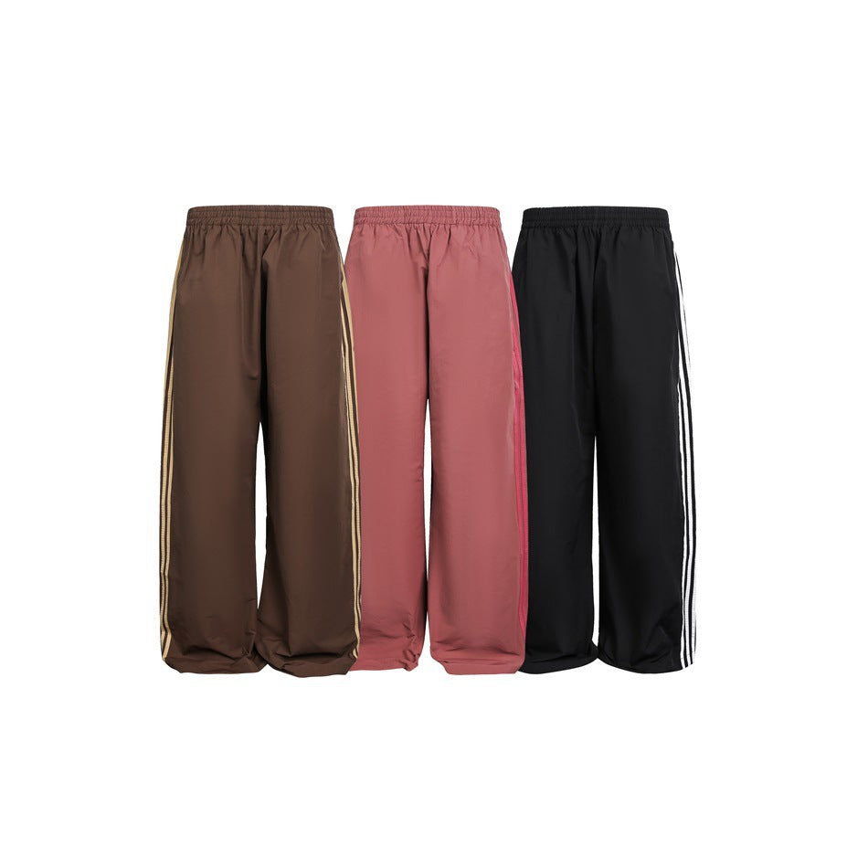 Three pairs of wide-leg track pants in brown, dusty rose, and black, each with contrasting side stripes.