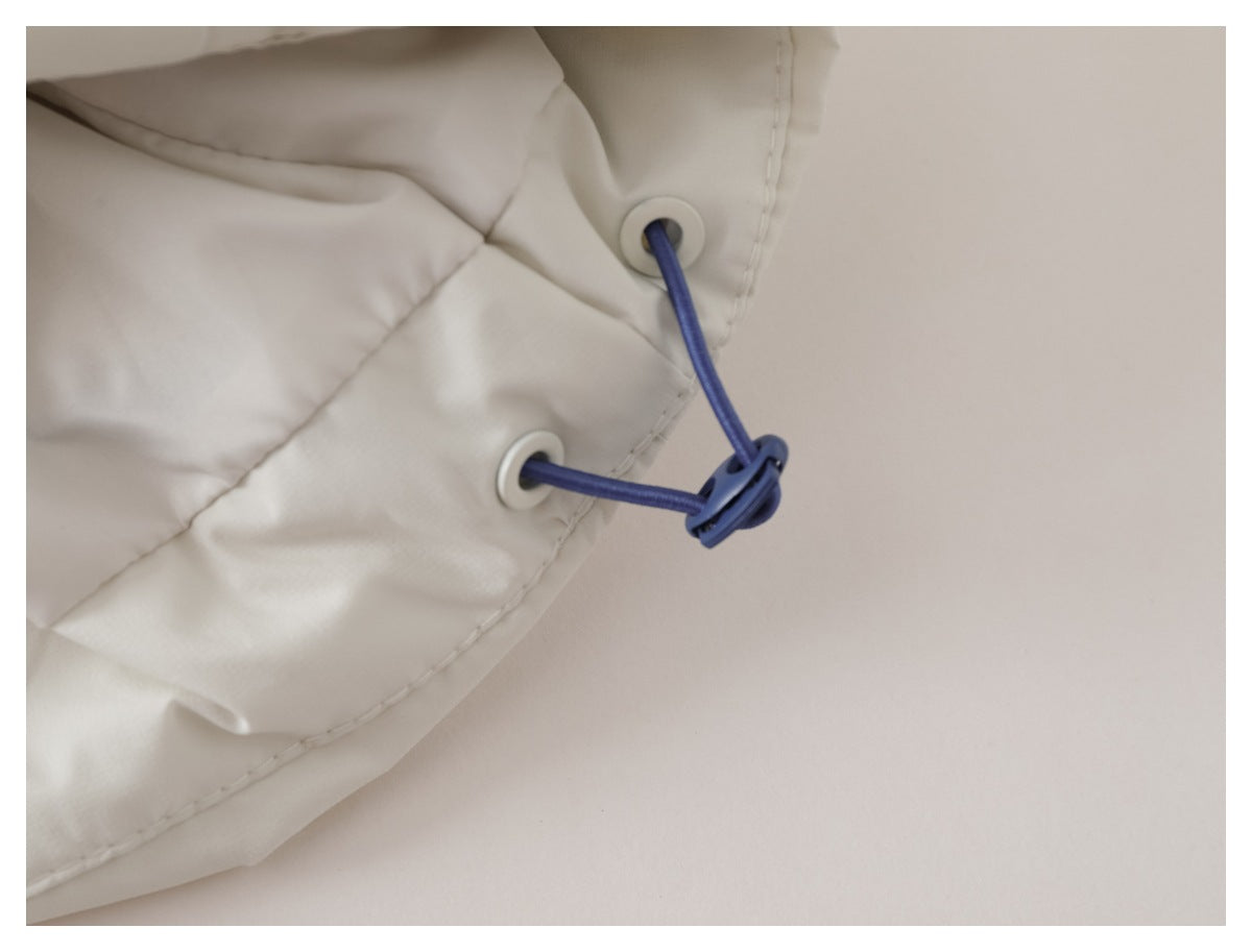 Close-up of a blue drawcord and toggle threaded through eyelets on a white quilted jacket.