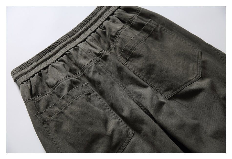 Close-up of dark olive pants showing the elastic waistband, stitching, and two patch pockets.
