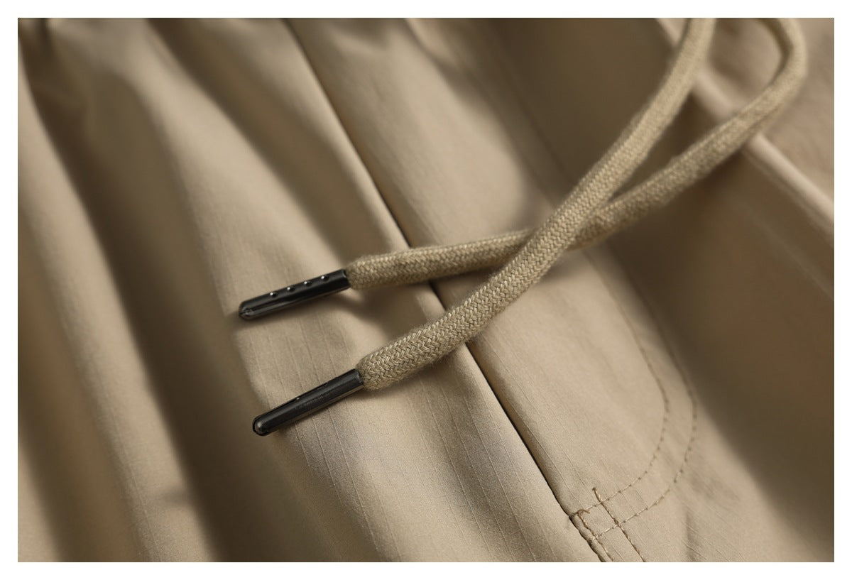 Close-up of tan fabric and braided drawstrings with dark metal tips.