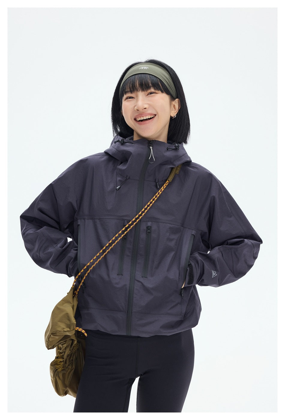 Close view of a model wearing a dark plum hooded jacket with a front zip and several zip pockets.