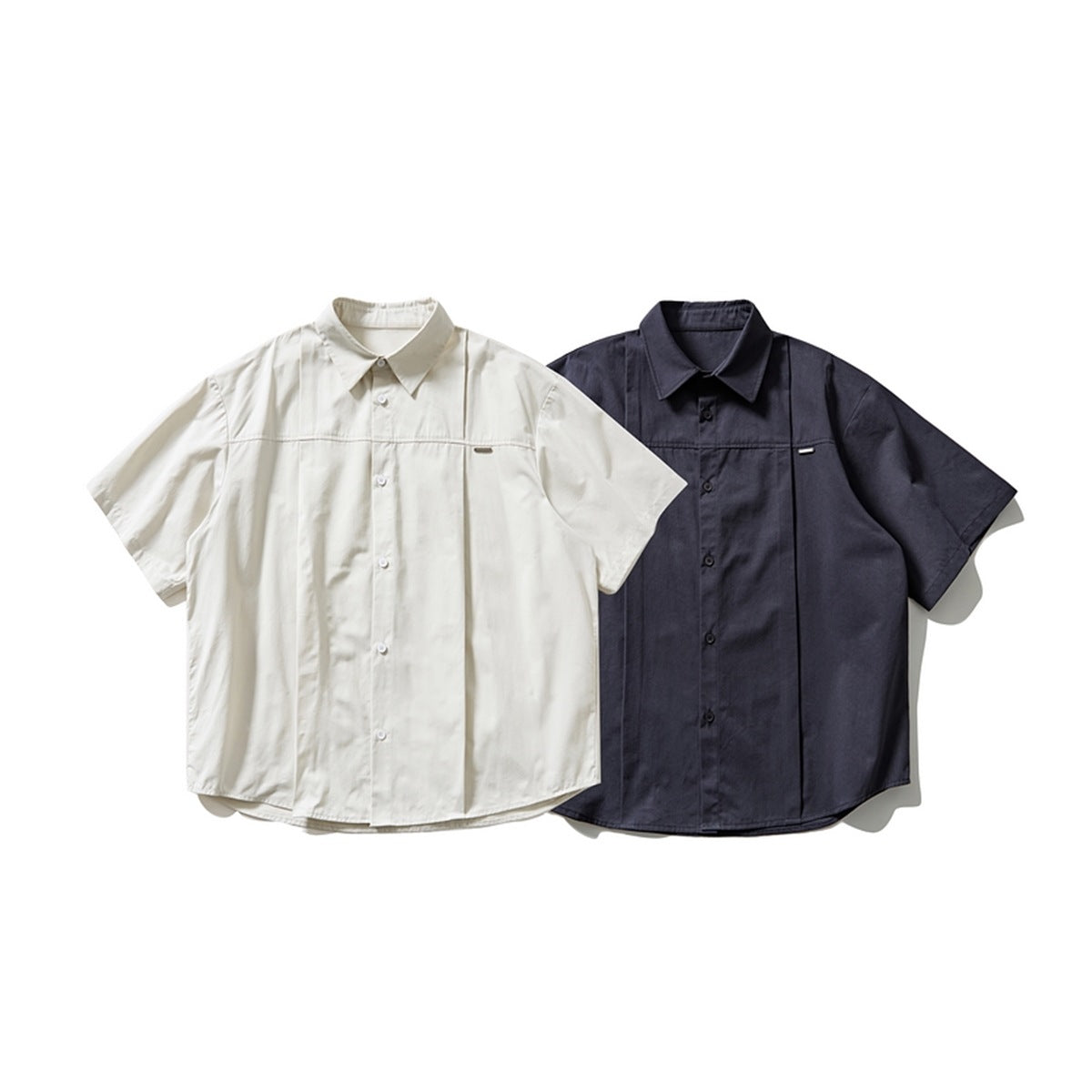 Two short-sleeve button-up shirts shown from the front: one ivory and one dark navy, each with a chest detail.