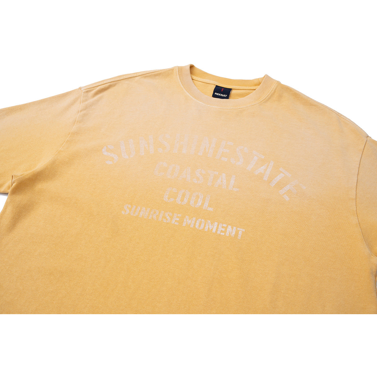 Close-up of a golden-yellow crew-neck T-shirt with pale text reading “Sunshine State, Coastal Cool, Sunrise Moment.”