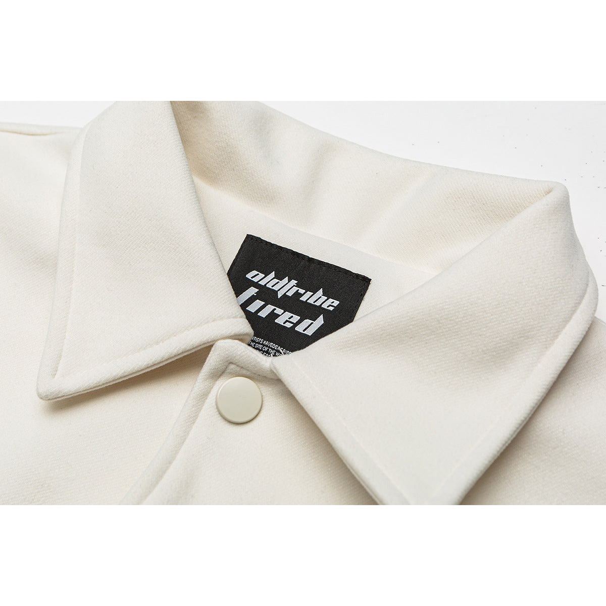 Close-up of an ivory jacket collar, showing a white snap and a black sewn-in neck label.
