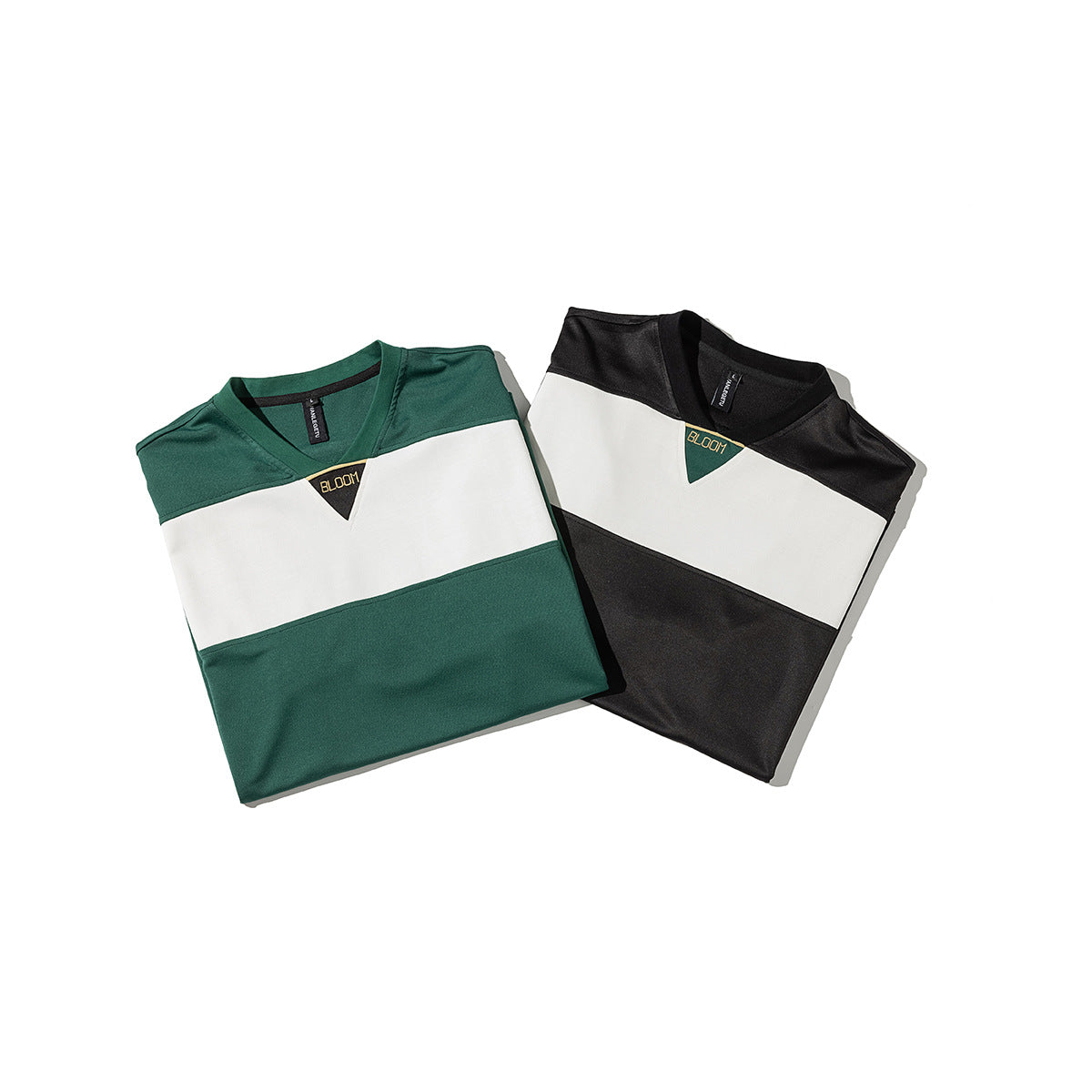 Two folded V-neck color-block shirts: one dark green and white, the other black and white, with small chest emblems.