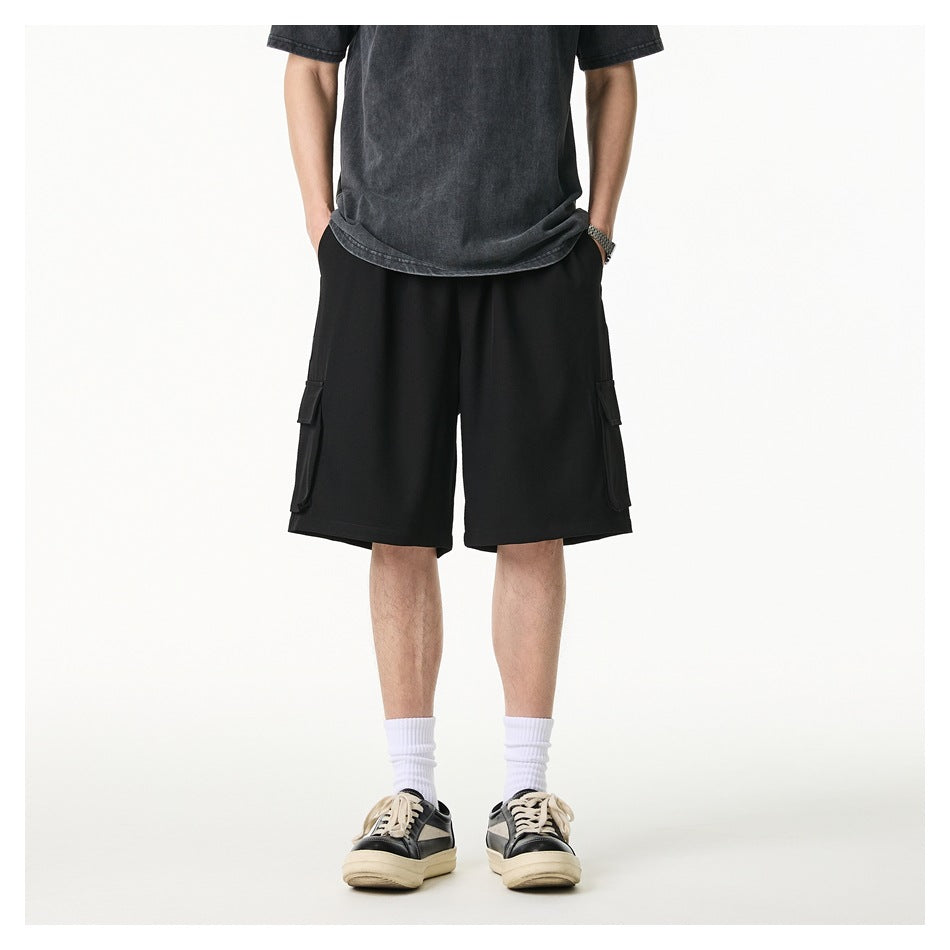 Front view of a model wearing loose black cargo shorts with flap pockets, a dark T-shirt, white socks, and sneakers.