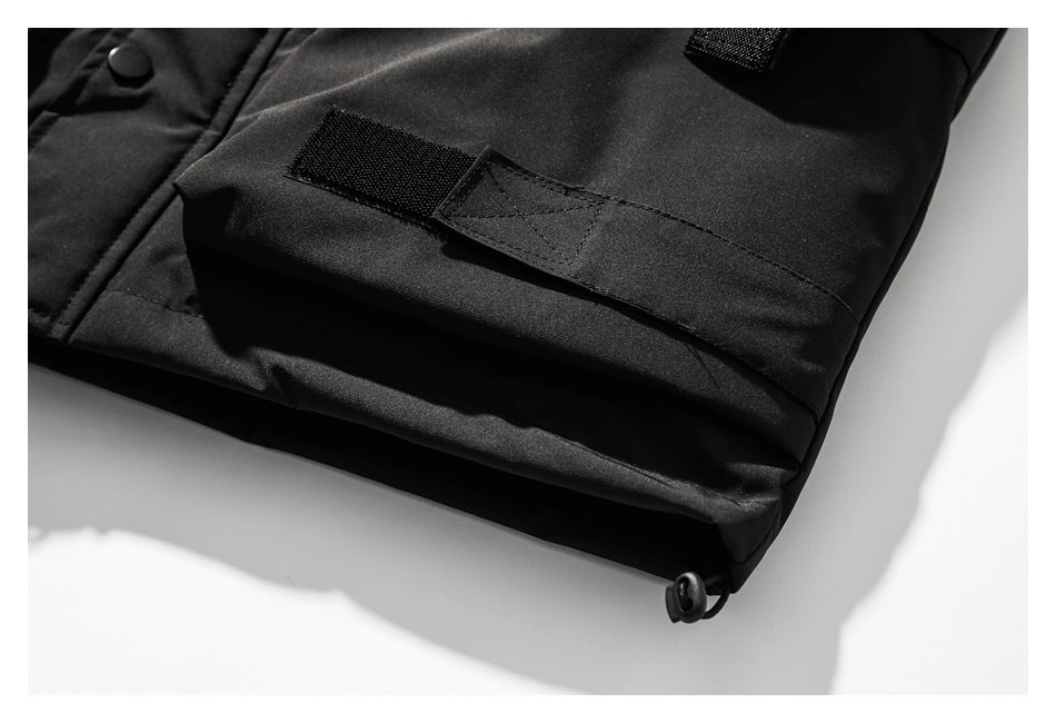 Close-up of a black garment hem with a hook-and-loop tab, snap fastener, and adjustable cord toggle.