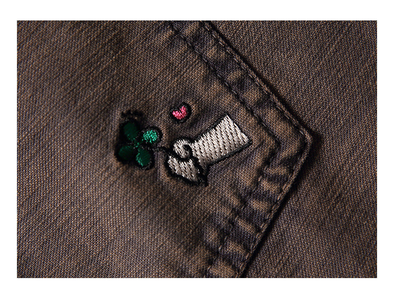 Macro view of a small green, pink, and white embroidered motif on brown textured fabric.