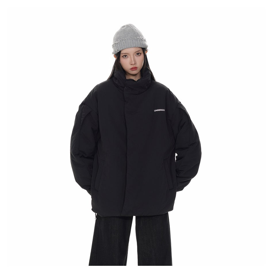 Front view of a model wearing an oversized black padded jacket with a high collar and small white chest lettering.