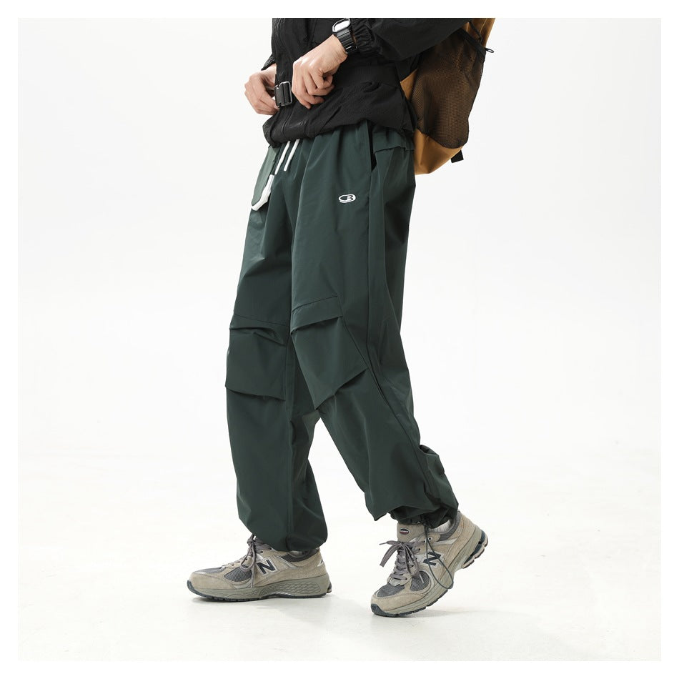 Angled view of a model wearing dark green wide-leg cargo pants with layered knee panels and a small logo.