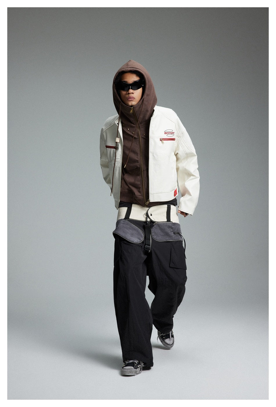 Model walking in the cropped white jacket over a brown hoodie with black pants, three-quarter front view