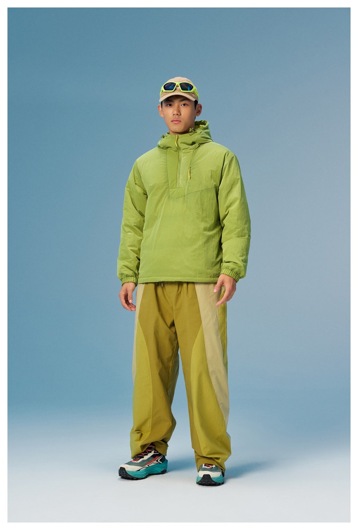 Full-length view of a model in a lime green grid-pattern hooded pullover and color-block outdoor trousers.