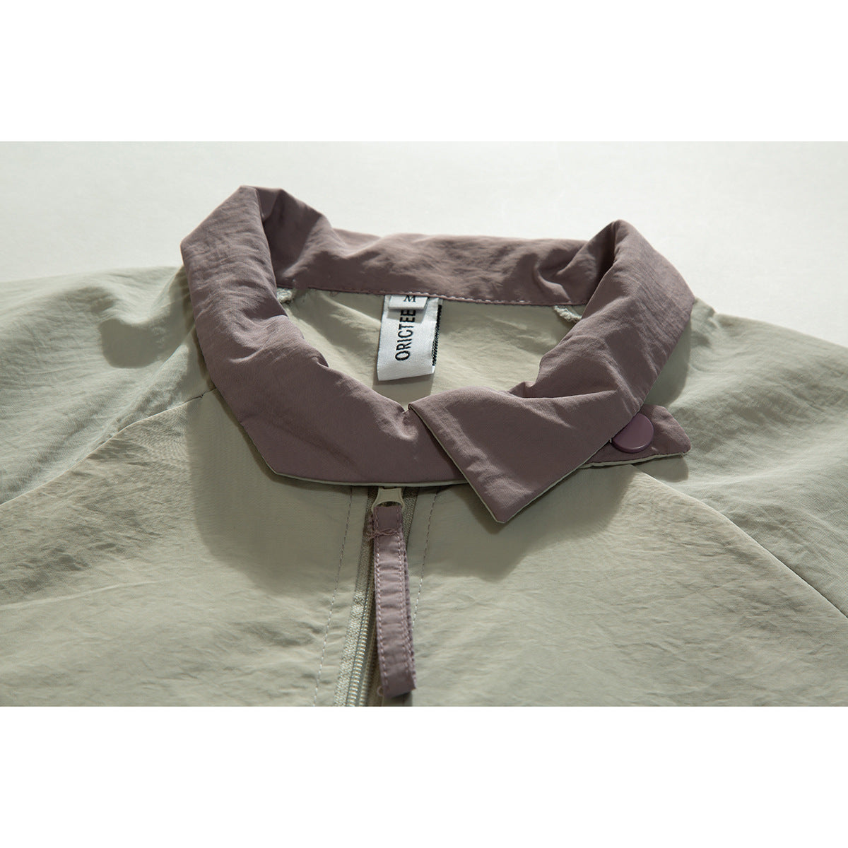 Close-up of a pale sage jacket with a wide dusty mauve collar, matching button and front zipper.