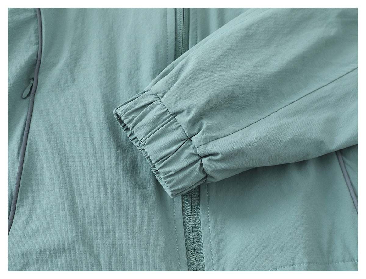 Close-up of a pale teal jacket showing the front zipper, gray piping, and gathered elastic sleeve cuff.