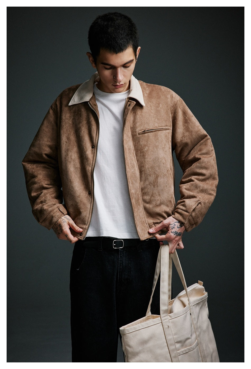 Front view of a man wearing a tan jacket with a cream collar and zip chest pocket, holding a cream tote bag.