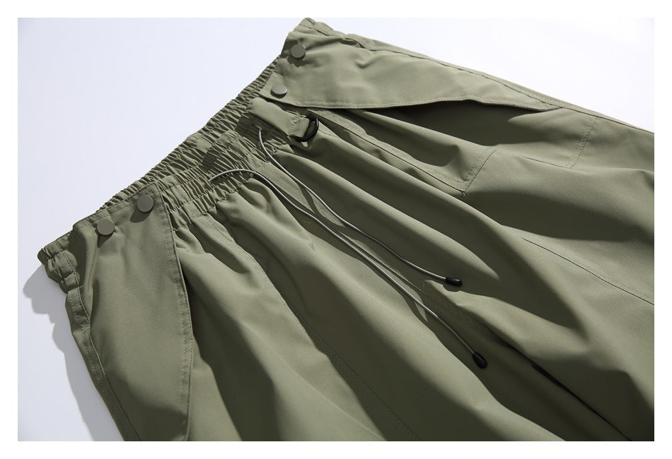 Close view of the olive-gray pants' gathered waistband, snap-button flap and adjustable drawcords.