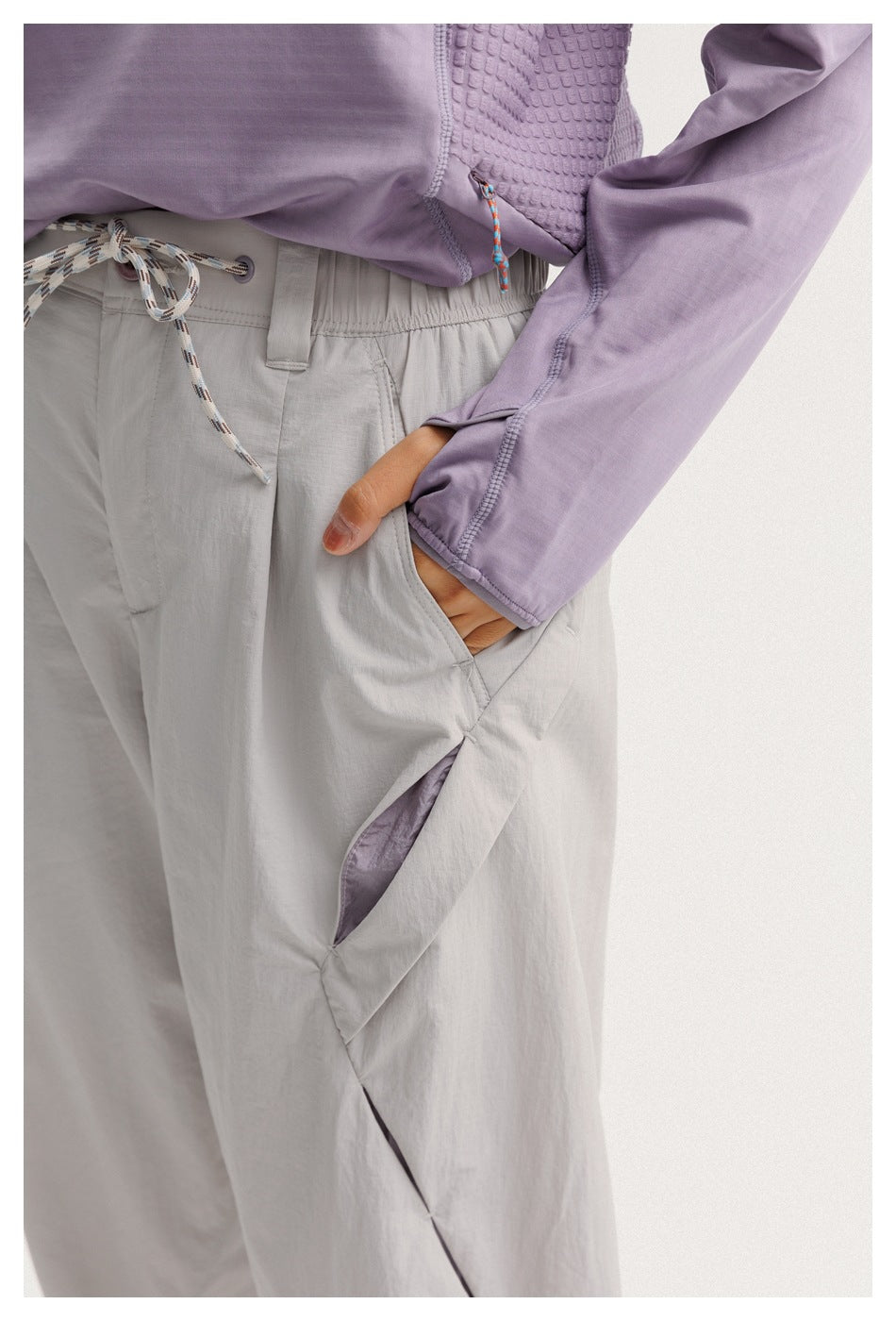 Close-up of light gray pants showing the drawstring waist and angled pocket, with the model's hand inside.