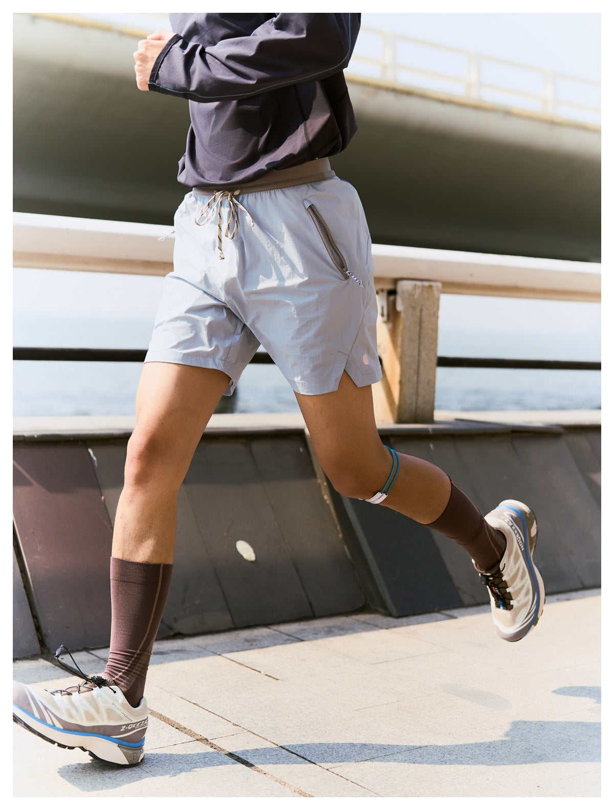 Side and rear view of a model running in pale gray drawstring shorts with a zippered pocket and side slits.