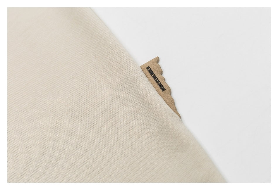 Close-up of beige T-shirt fabric with a small tan branded side tab.