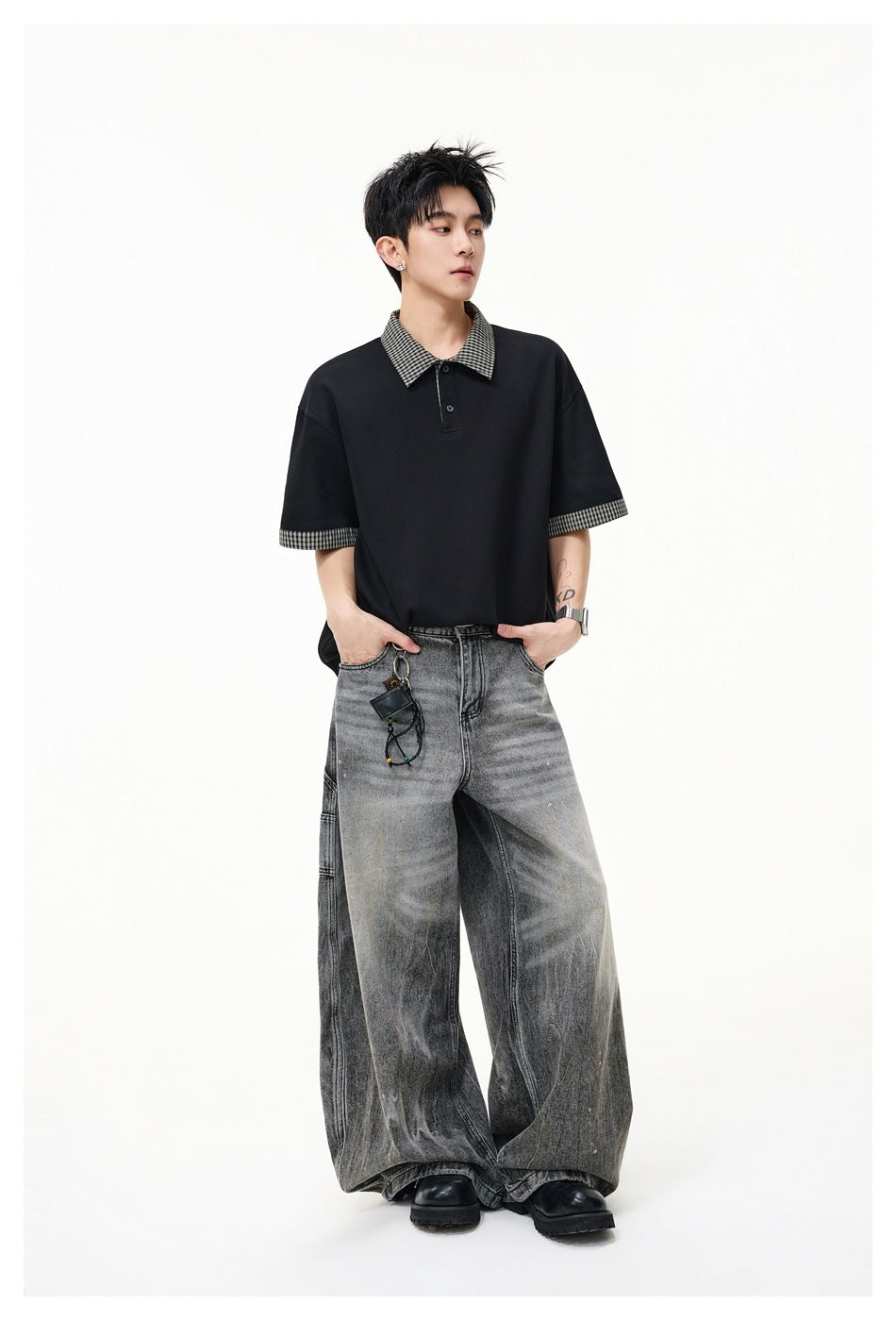 Full-length model wearing a loose black polo with checked collar and sleeve cuffs, paired with wide gray jeans.