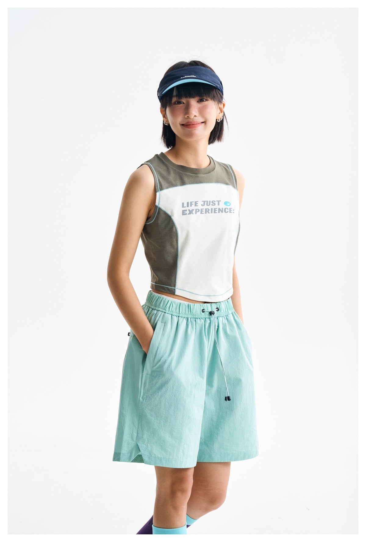 Model wearing a color-block sleeveless crop top with aqua piping and a mint skirt; front view.