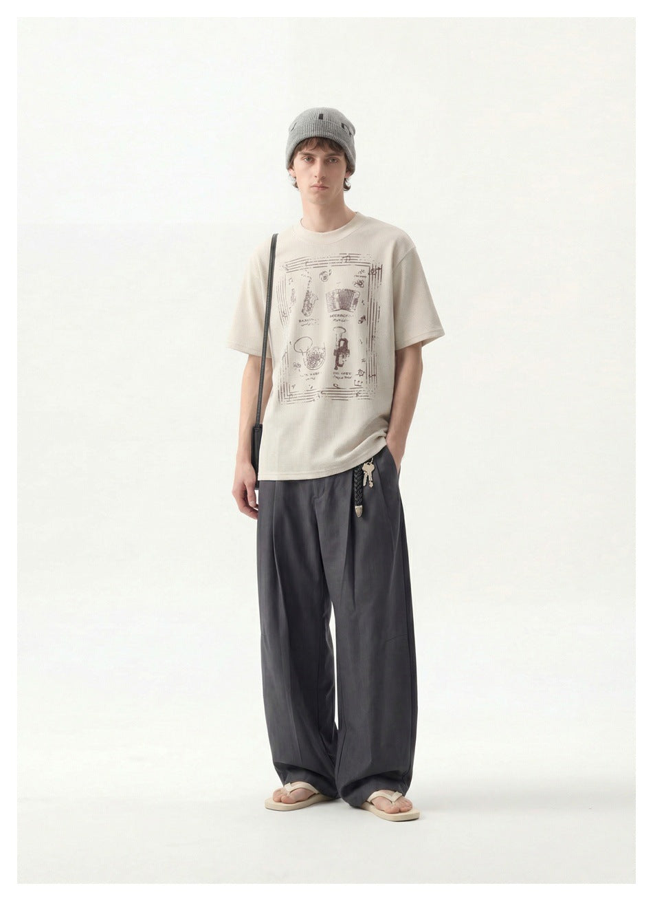 Model wearing a beige graphic T-shirt with gray wide-leg trousers, a gray beanie and sandals, full-length view
