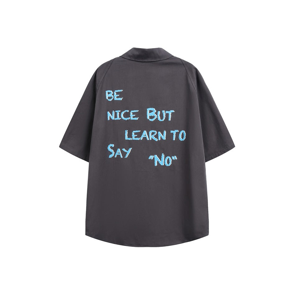 Back of dark gray short-sleeve shirt with light blue textured 'BE NICE BUT LEARN TO Say NO' lettering