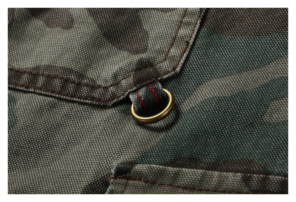 Close-up of a brass-colored D-ring attached beside a pocket on camouflage fabric.