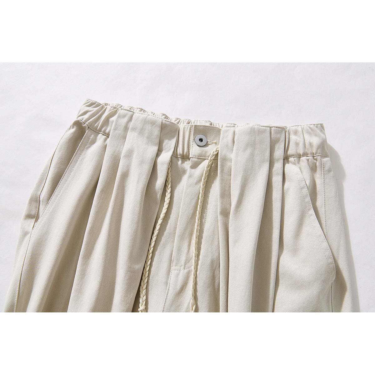 Close-up of ivory wide-leg pants showing a gathered waistband, front button, pleats and braided drawstrings.