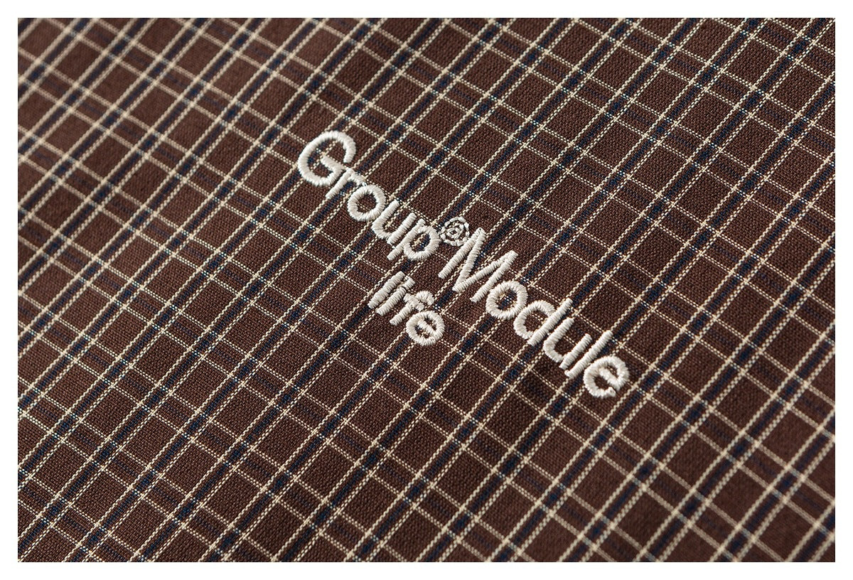 Close-up of white embroidered lettering on brown plaid fabric.