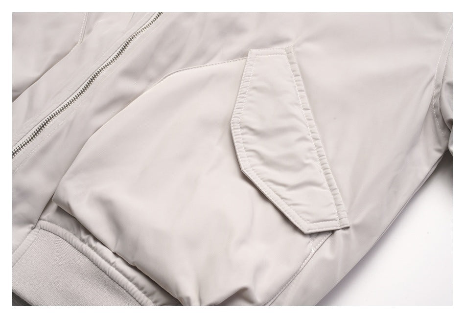 Close-up of a pale gray jacket's flap pocket and ribbed hem beside the front zipper.