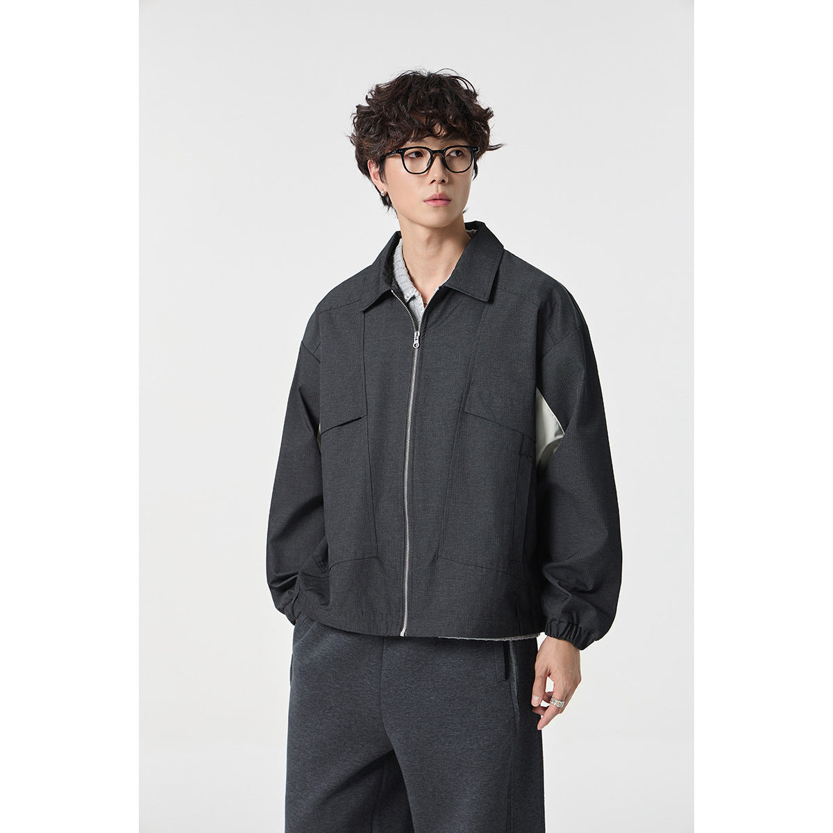 Closer view of a model wearing a charcoal zip-front jacket with a pointed collar, roomy sleeves and patch pockets.