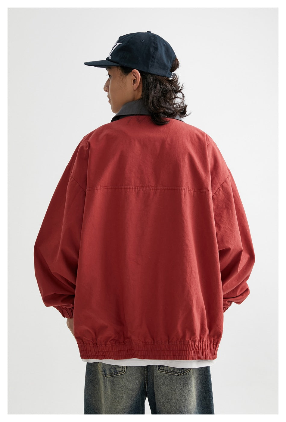 Rear view of a model wearing a plain rust-red jacket with a gray collar and gathered elastic hem.