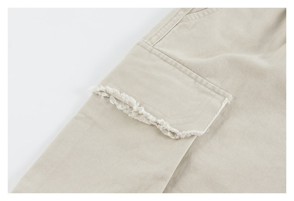 Close-up of a flap pocket with a frayed edge on beige shorts.