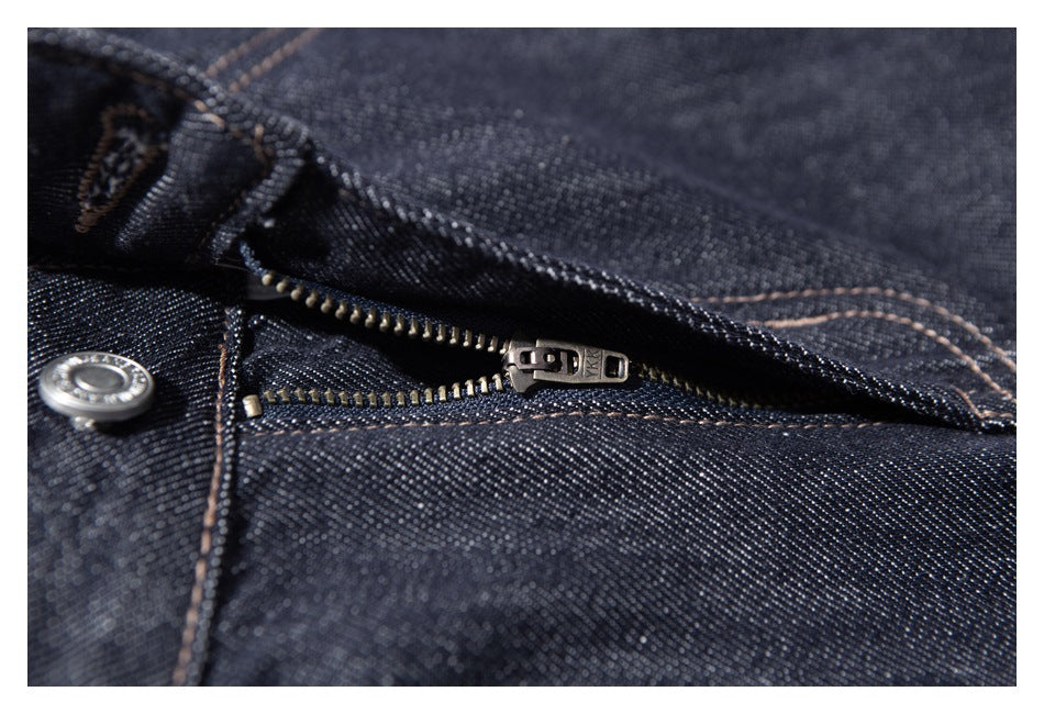Close-up of dark indigo denim with an open metal zipper, button and tan contrast stitching.