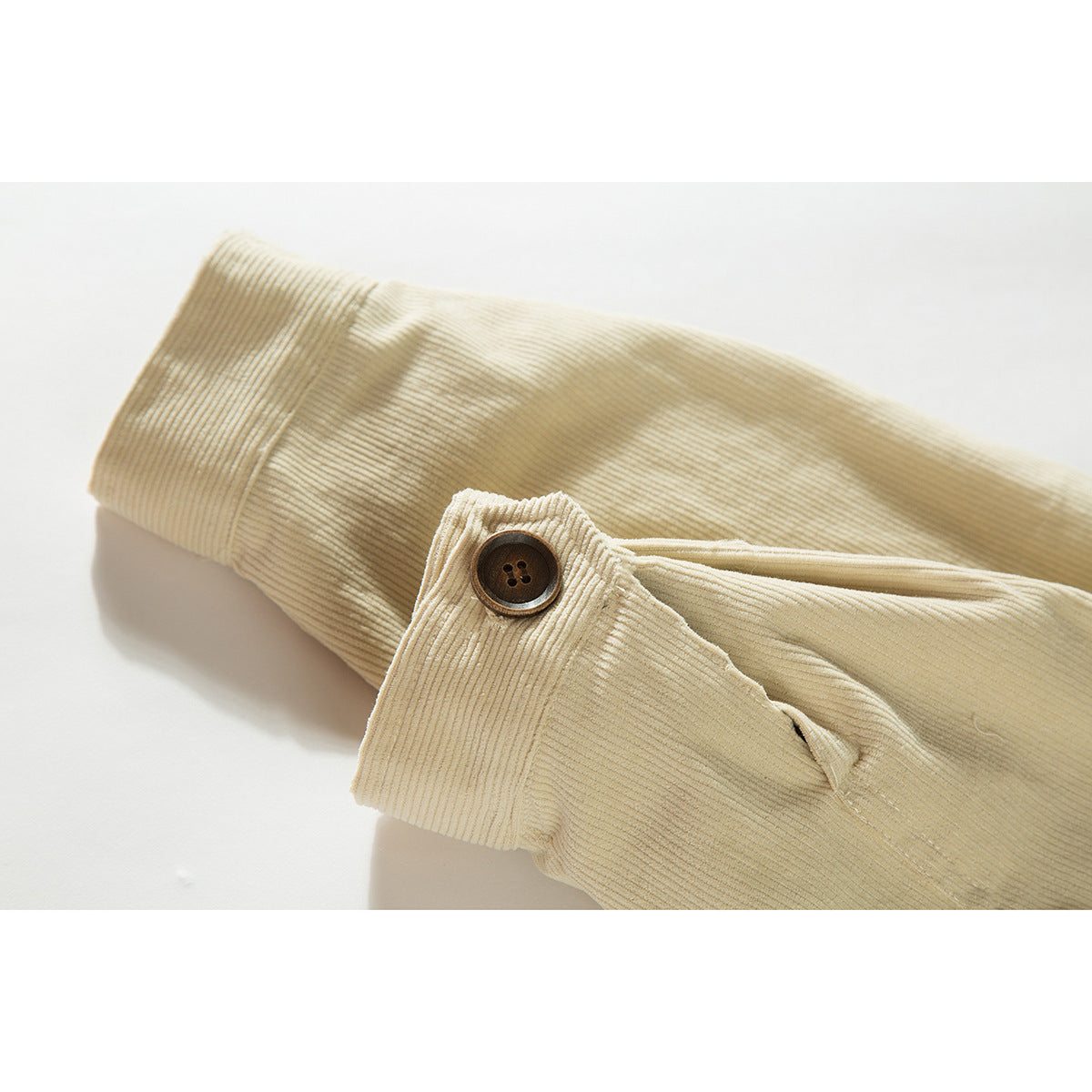 Close-up of a cream ribbed jacket sleeve cuff with a dark button and seam detail.