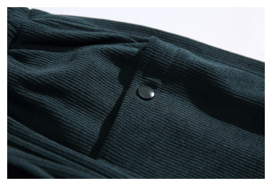 Close-up of a snap-button pocket on the dark teal pants, showing the ribbed surface and stitching.