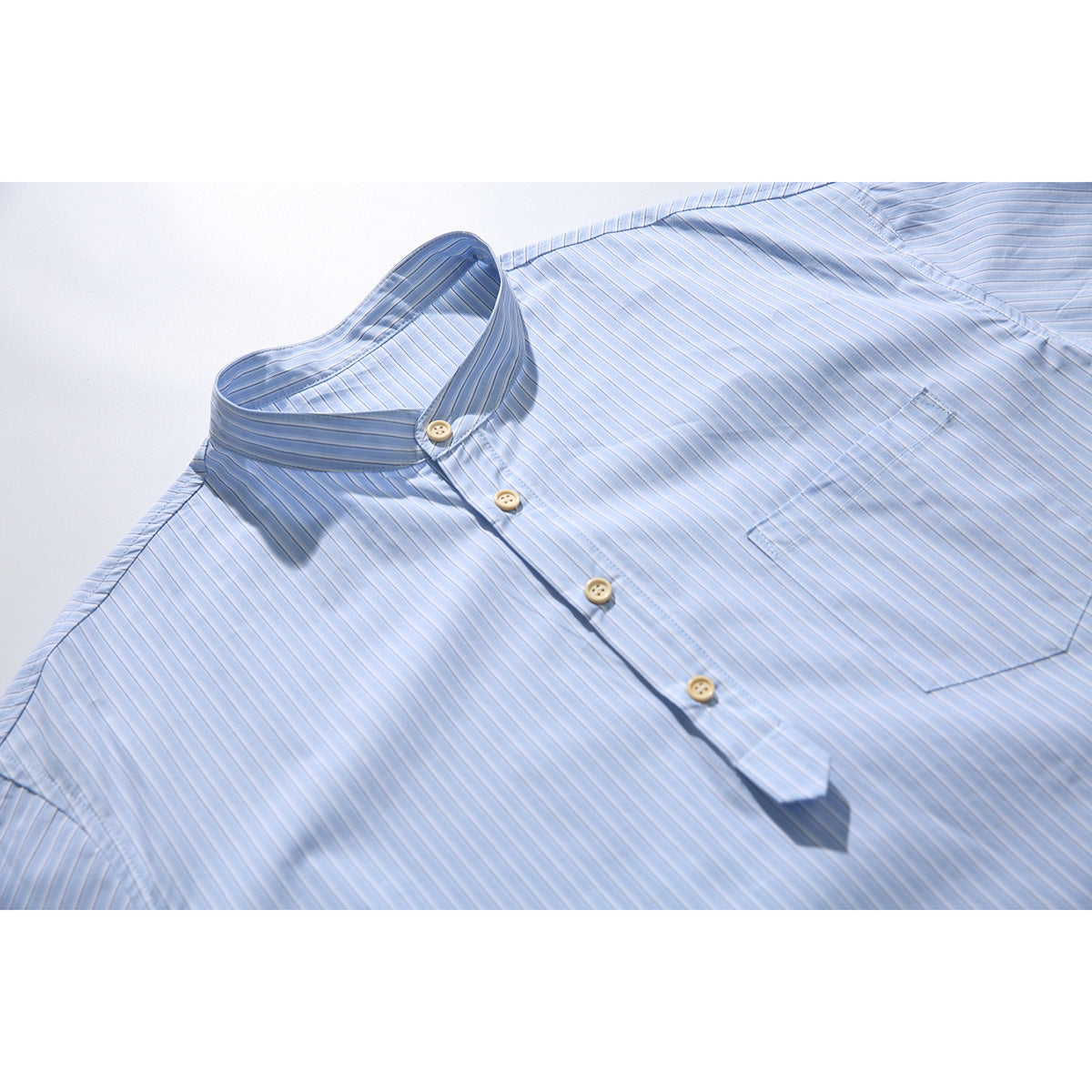 Light blue finely striped shirt laid flat, showing its stand collar, button placket and chest pocket.