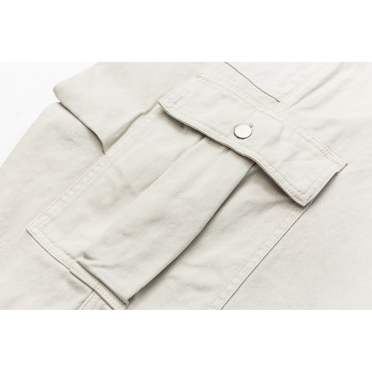 Close-up of an off-white shorts pocket flap with a silver snap and stitched seams.