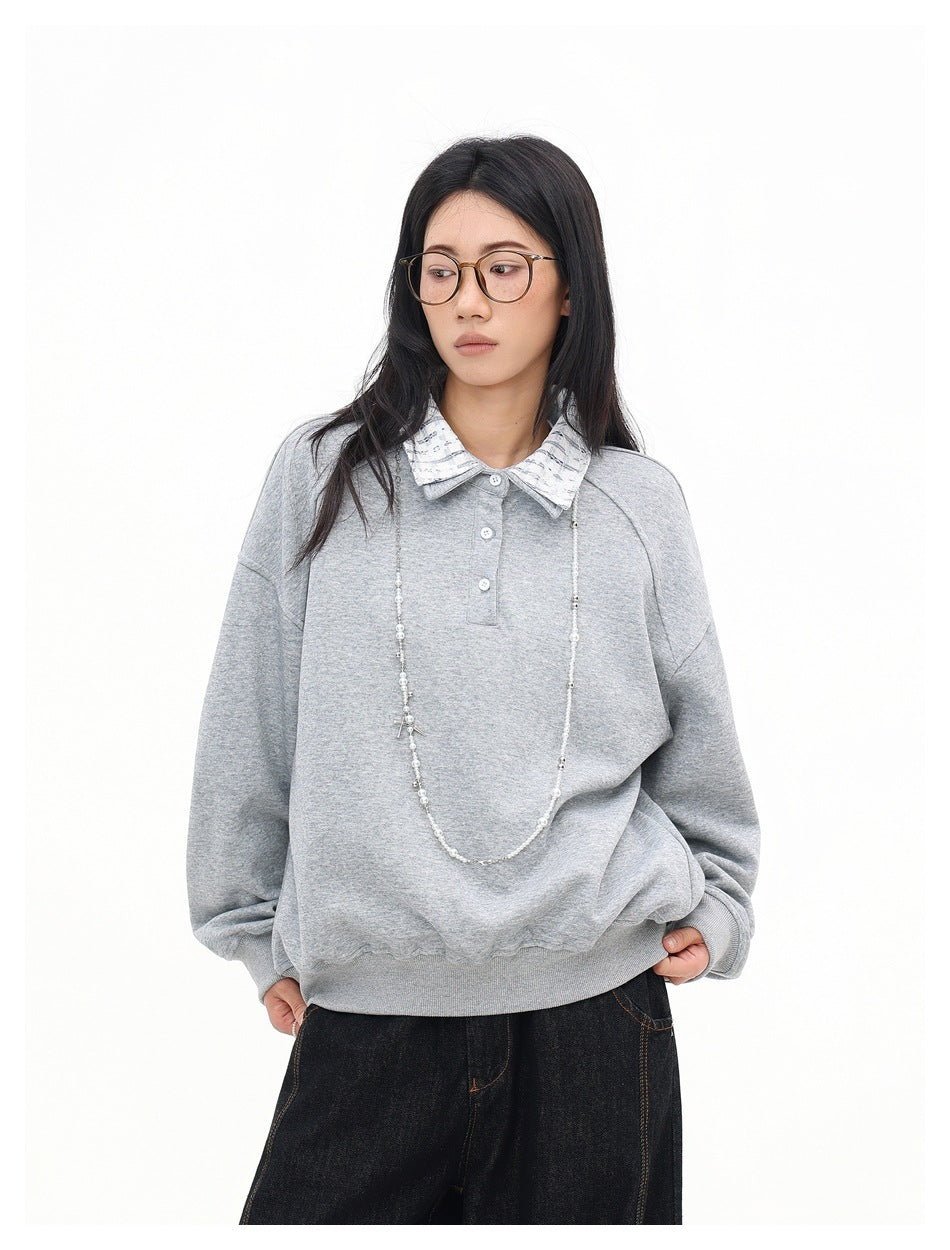 Closer view of a model wearing a light gray pullover with a patterned collar, button placket, and long necklace.