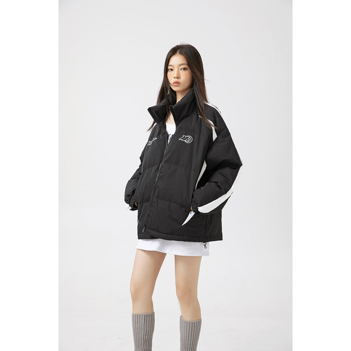 Front view of a model wearing a black padded jacket with white sleeve stripes, a high collar and chest graphics.