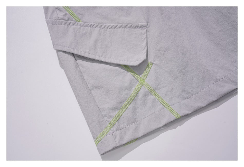Close-up of light gray bottoms showing a flap pocket and lime green cross-stitching.