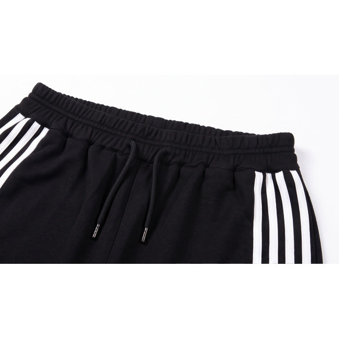 Close-up of black pants with an elastic waistband, black drawstrings, and white side stripes.
